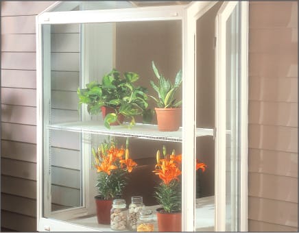 A Keystone Window garden window extends from a house wall, filled with vibrant houseplants and flowers, offering a miniature greenhouse effect for the home interior.