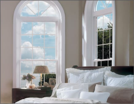 Elegant bedroom featuring a tall Keystone double hung window with an arched transom, flooding the room with natural light and offering a serene sky view.