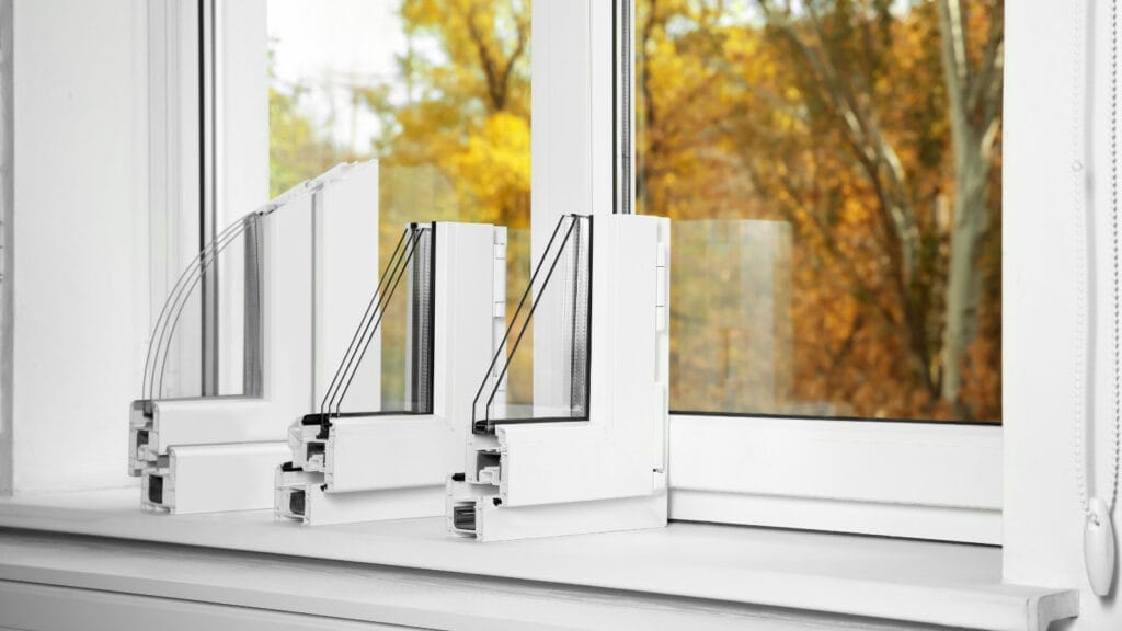 Cross-section view of triple and double pane window models showcasing insulation efficiency, with autumn trees in the background.