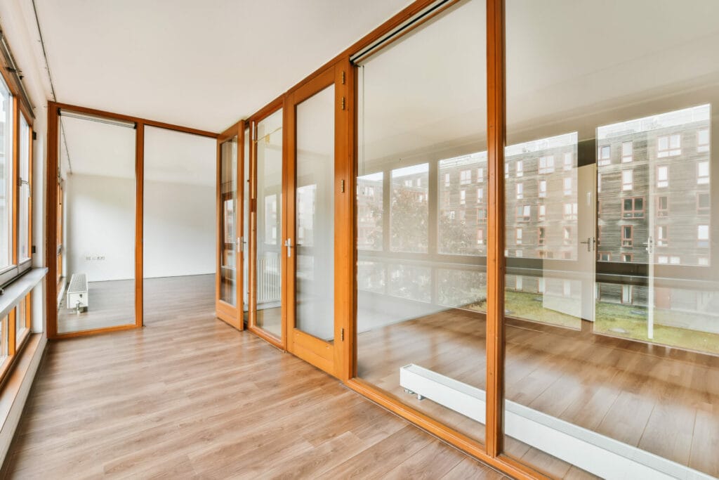 Spacious room with polished wooden floors and a series of sliding patio doors by Keystone Window, offering a seamless transition to the outside environment