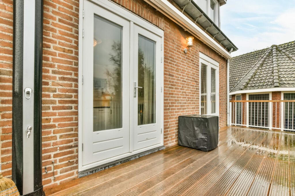 French patio doors set in a classic brick home open onto a wooden deck, showcasing the elegant design and craftsmanship of Keystone Window installations Comment end