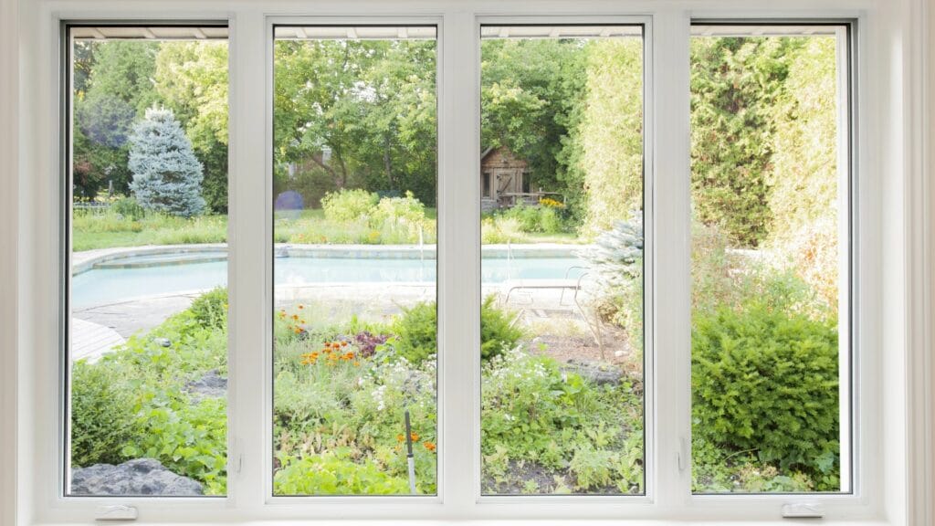 View through energy-efficient triple-paned windows showing a lush garden with a variety of plants and a swimming pool, exemplifying potential energy savings in a home setting.